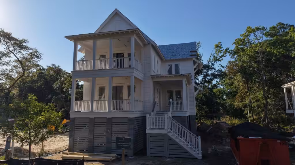 Two-story elevated home with stacked covered porches and white railings across the front, white lap siding and a piered foundation