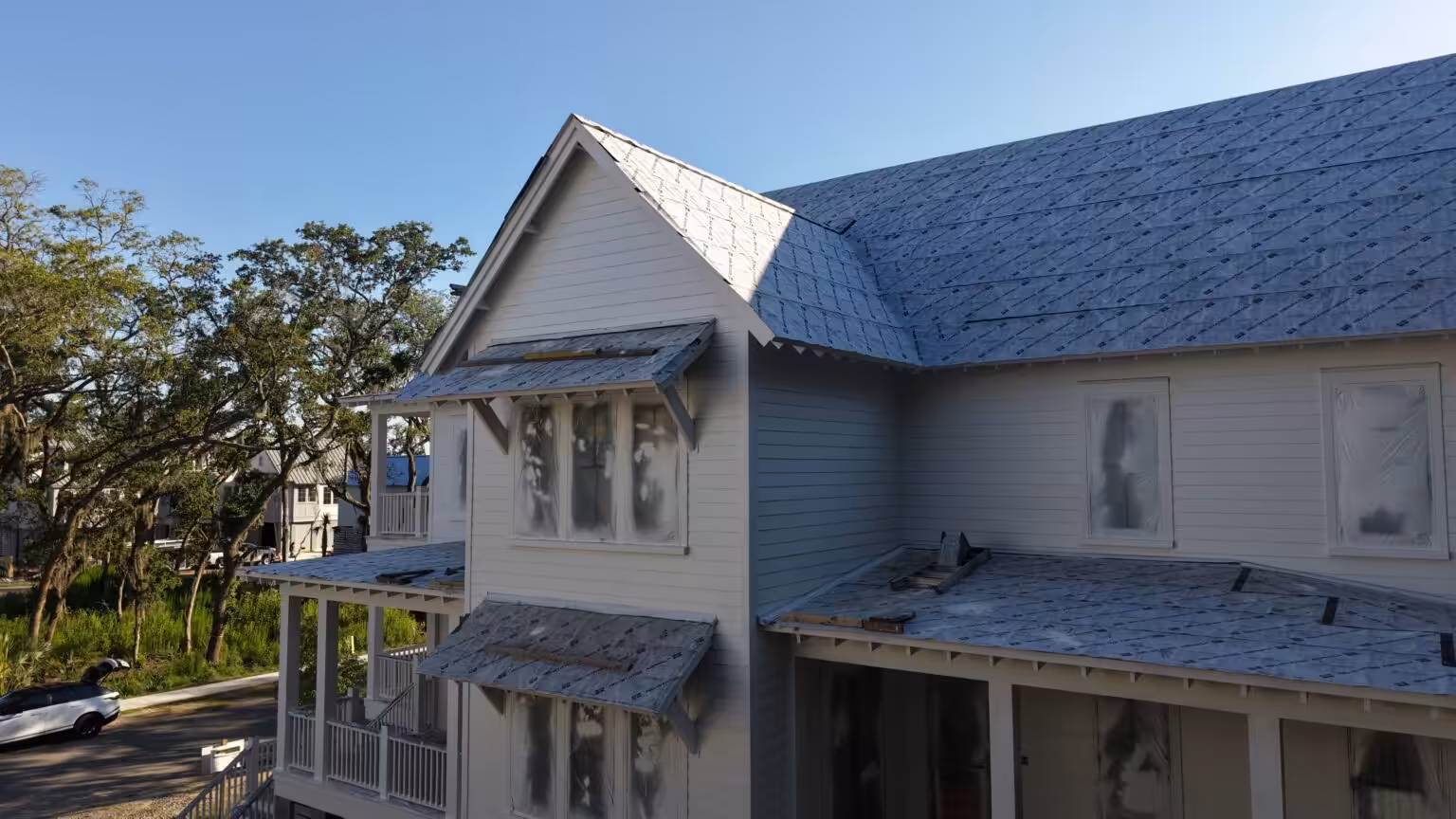 Roofs in underlayment meeting the white lap-sided walls of a two-story elevated home with porches