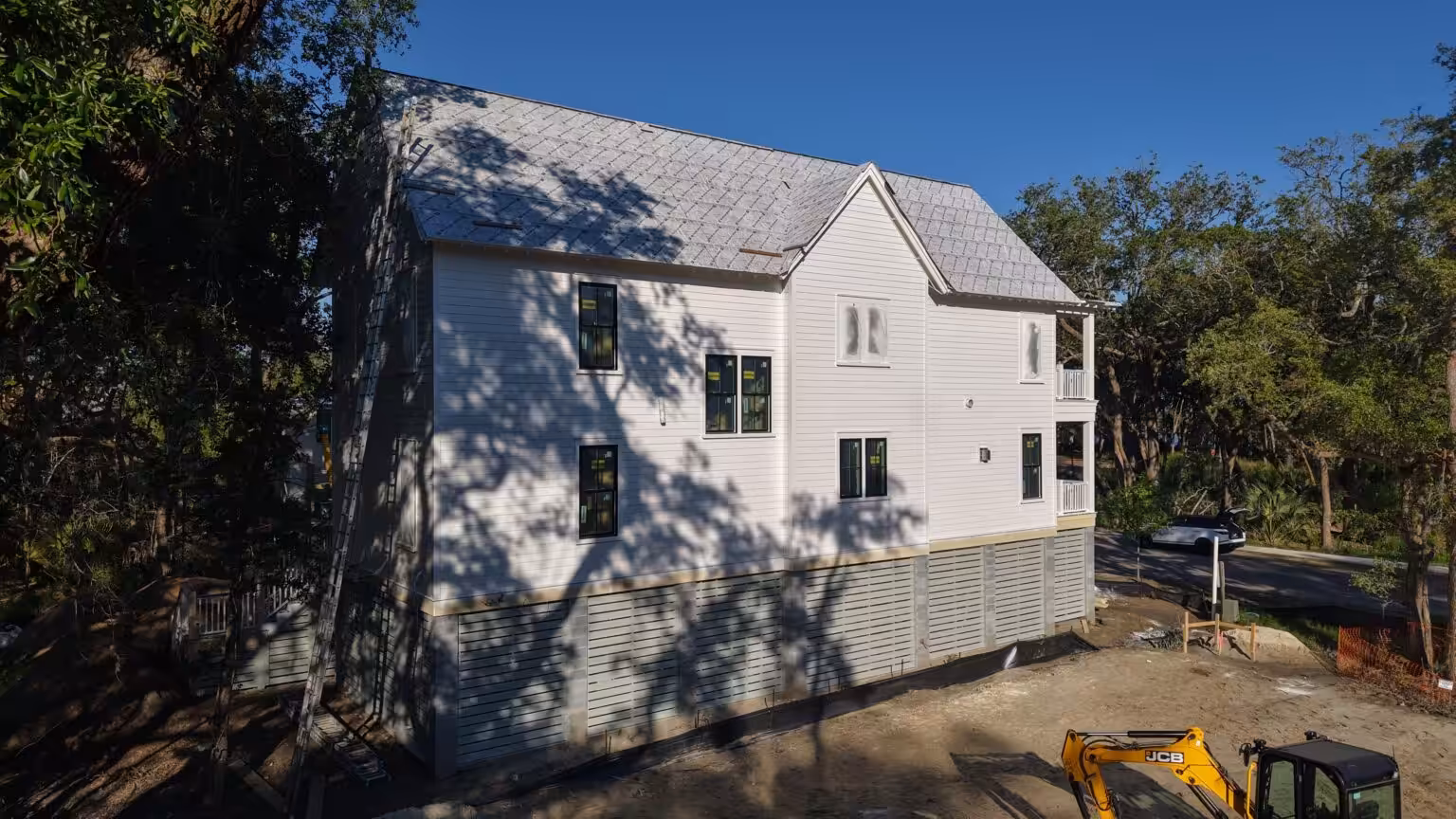 Side elevation of a new elevated home with white lap siding, black-framed windows and a slatted skirt over the piers