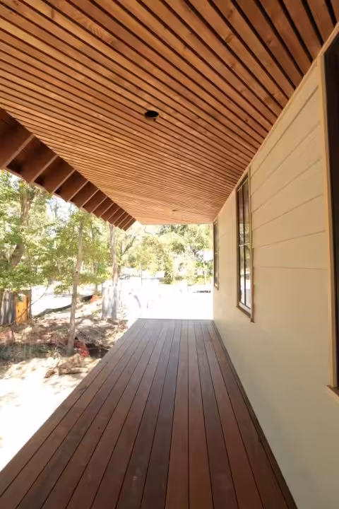 Long covered porch with dark deck boards, a wood slat ceiling and lap siding on the house wall