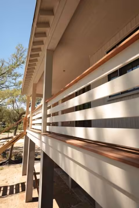 Porch railing of white horizontal boards topped with a natural wood cap rail, under a white porch ceiling and eave